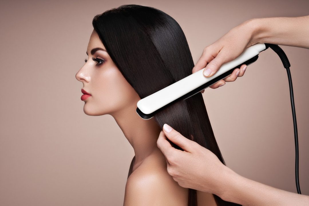 hairdresser straightening long hair with hair irons