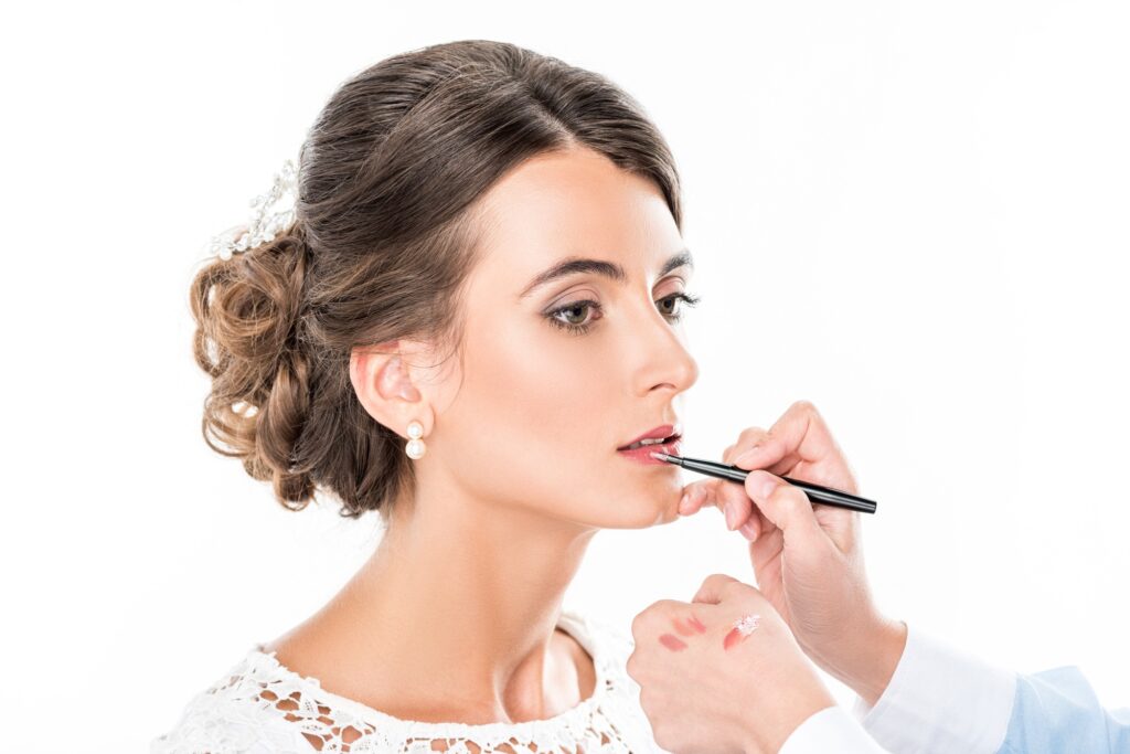 side view of makeup artist applying lipstick on models lips using lip brush isolated on white